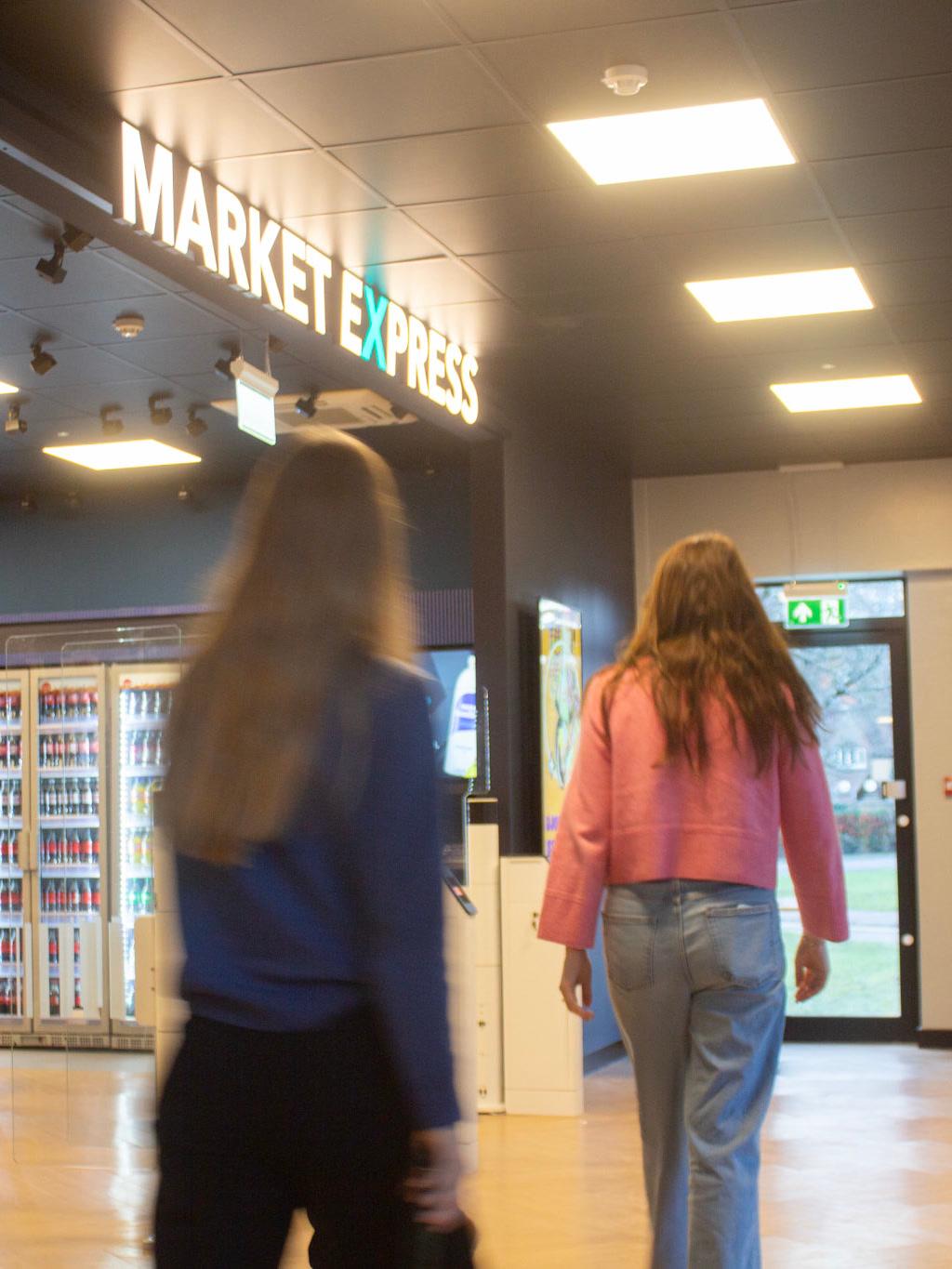 Two shoppers walking into a convenience store, one caught in motion blur